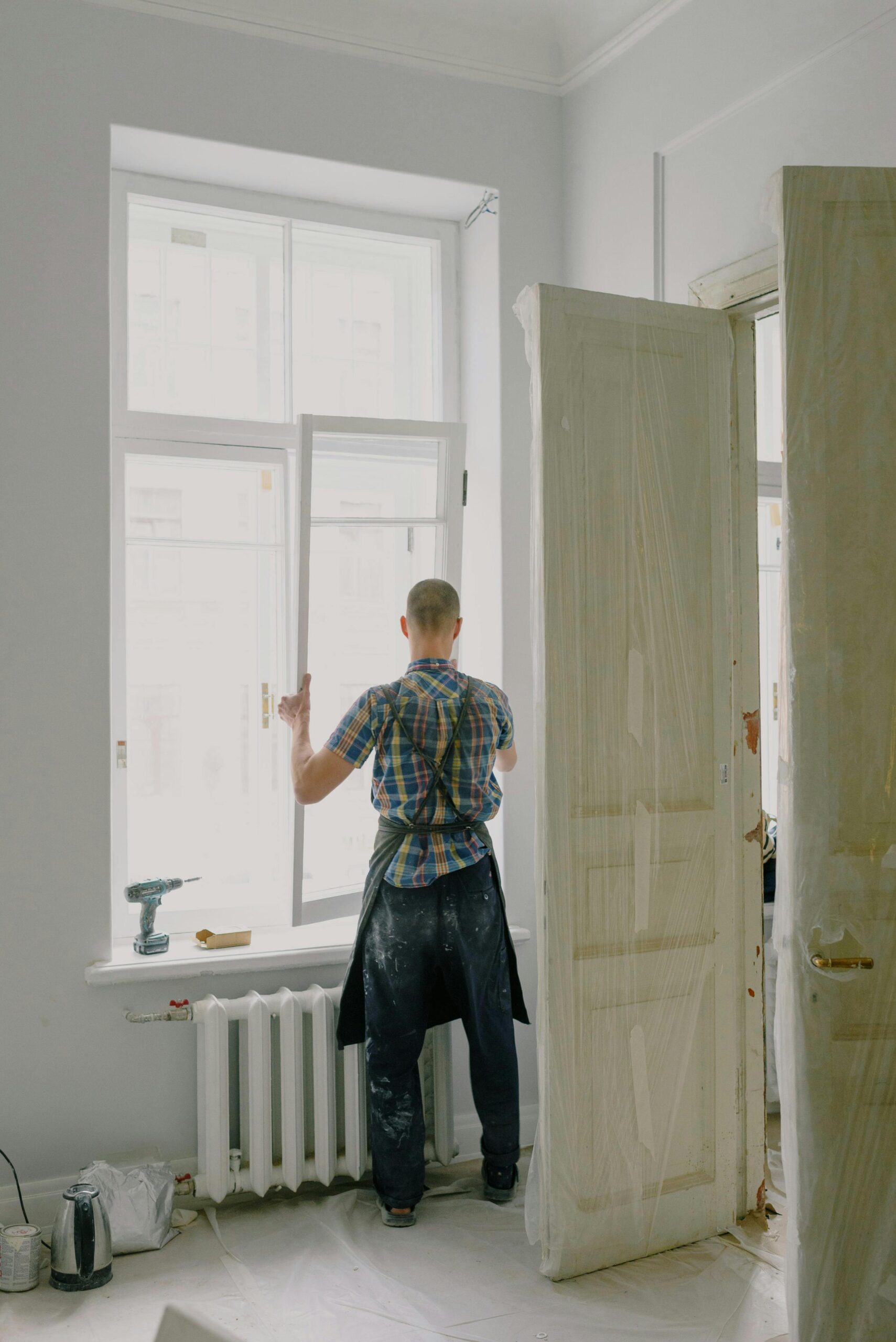 Full-length view of a handyman fixing a modern window in a bright room.